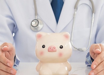 Closeup of a doctor with a piggy bank on a table.