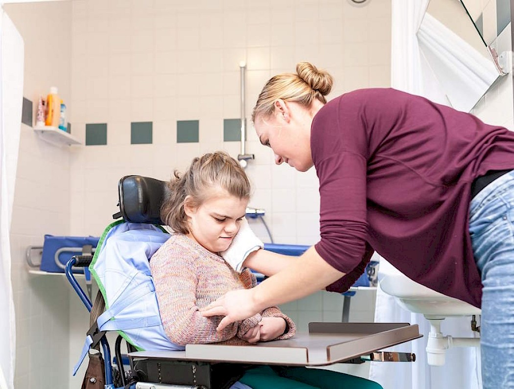 A carer helping a young disabled girl who is in a wheelchair.