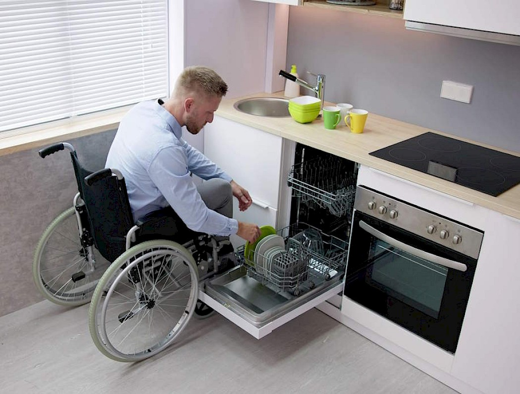 A man in a wheelchair struggling to load his dishwasher due to a lack of essential adaptations in his home that could be provided by the Disabled Facilities Grant.