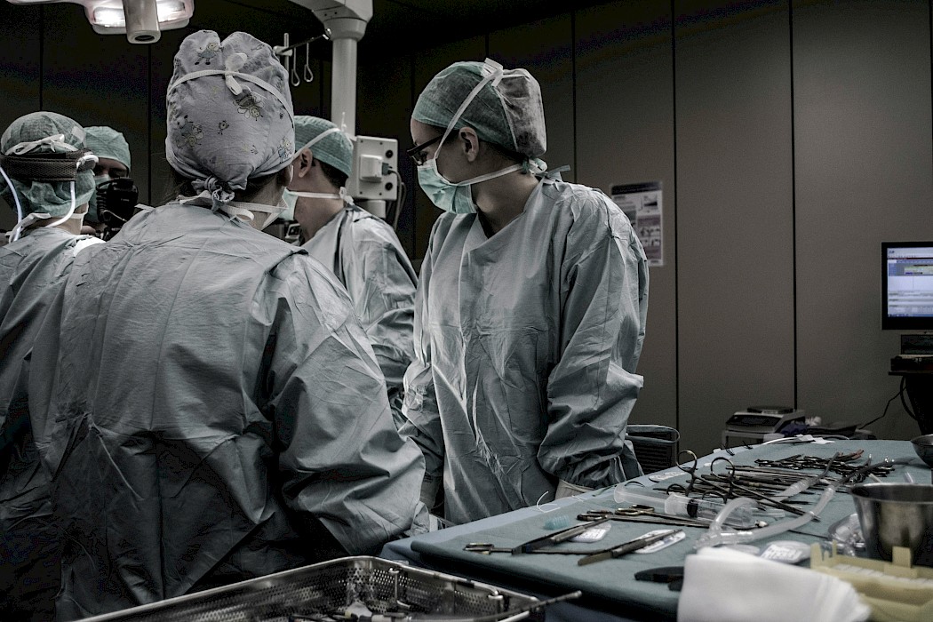 5 surgeons stood around an operating table wearing PPE.