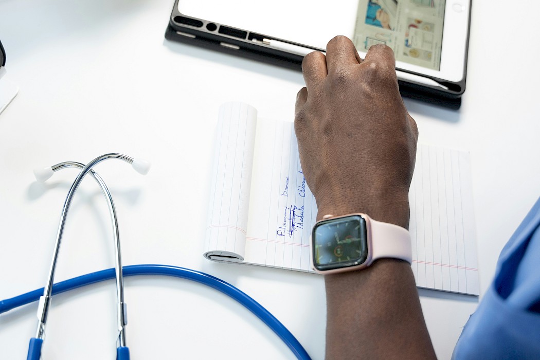 Doctors hand wearing a smart watch, making notes on paper and a smart tablet.