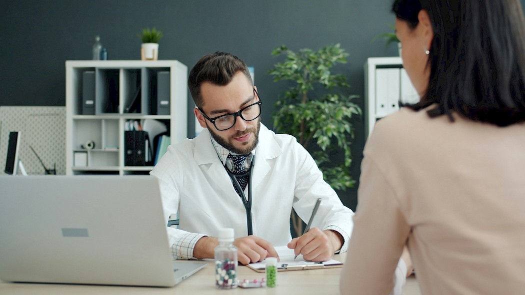 Male doctor writing notes while talking to a female patient.